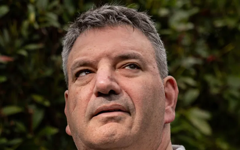 Andrew Franks photographed outdoors in front of green leaves.