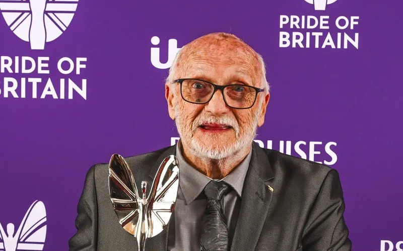 Barry Walden holding his Pride of Britain trophy in front of a Pride of Britain backdrop.