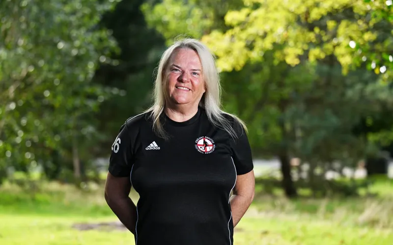 Elaine Oakey in a black football shirt, standing on grass in a park.