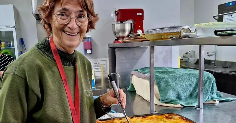 Jenny Kearney smiling in a kitchen, wearing a green jumper and a red lanyard.